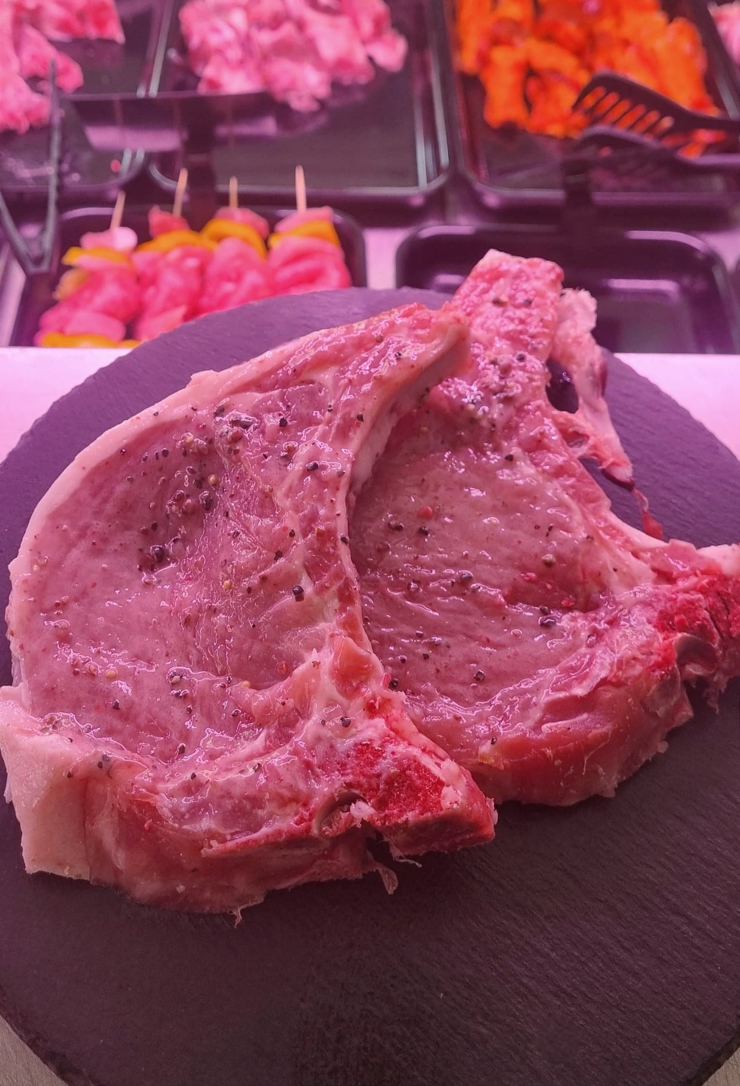 Fresh pork chops on a slate plate, showcasing tender meat ready for cooking with a vibrant market background.