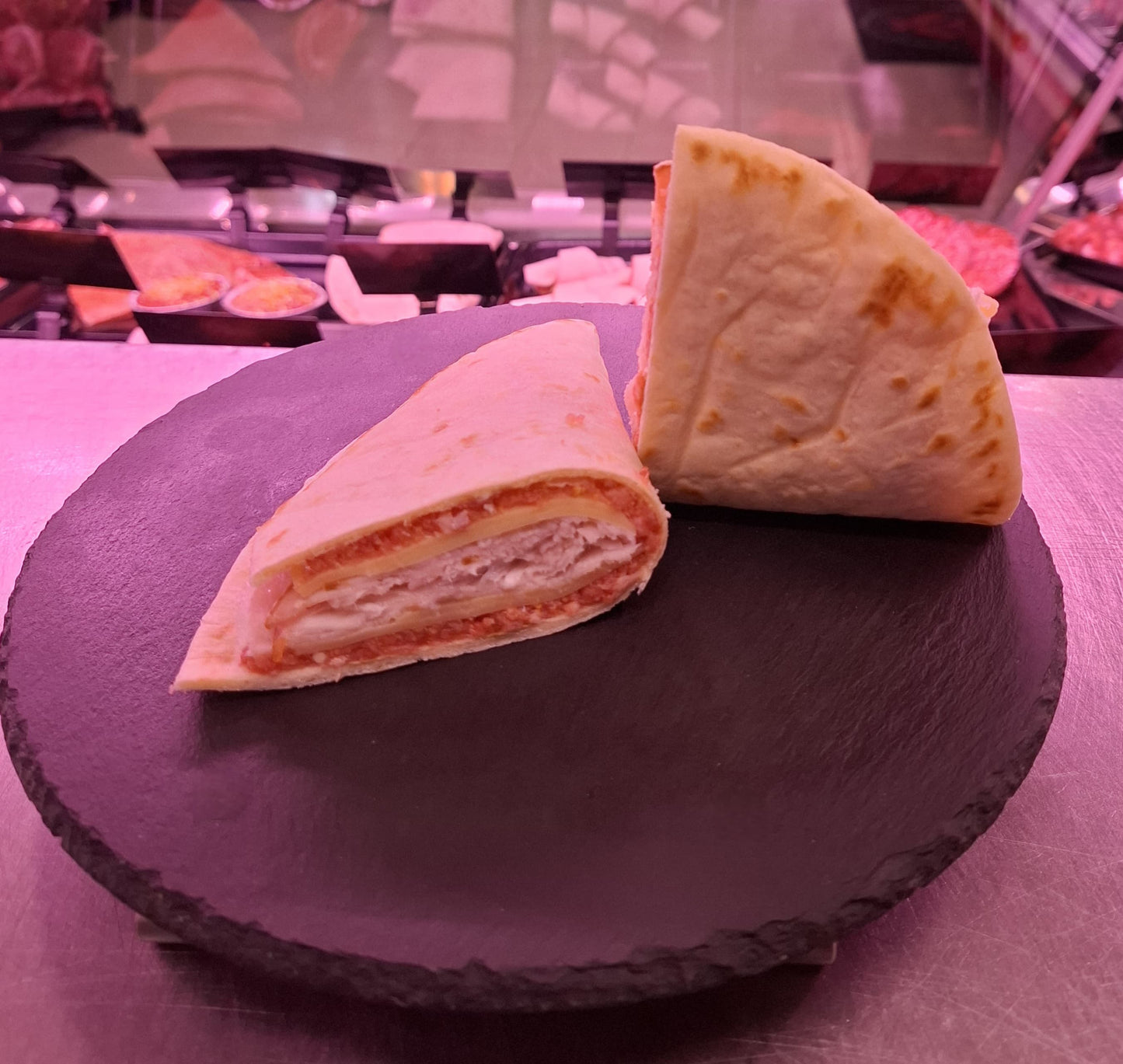 Delicious piadina ripiena filled with artisan porchetta and emmental on a black slate plate.