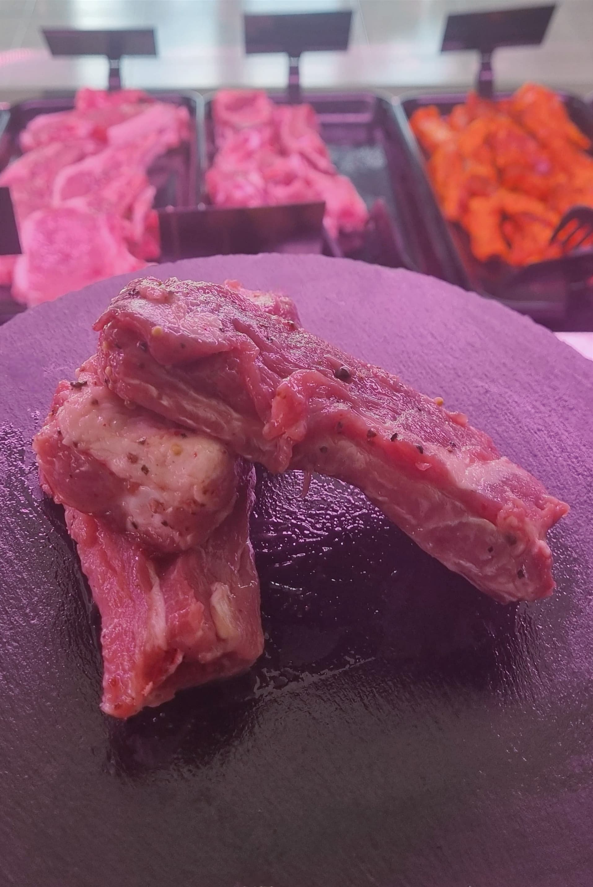 Costine di maiale succulente su un piatto nero, pronte per la cottura e condite con pepe rosa.