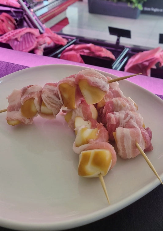 Uccelletti pugliesi con scamorza avvolti in pancetta su uno spiedino, serviti su un piatto bianco.
